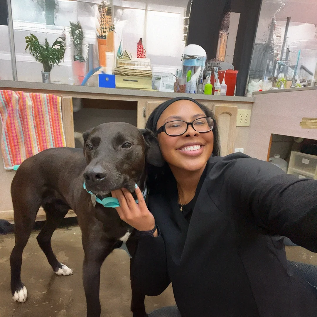 Receptionist Alina smiling and taking a selfie with a black dog wearing a teal collar inside Animal Medical and Surgical Hospital.