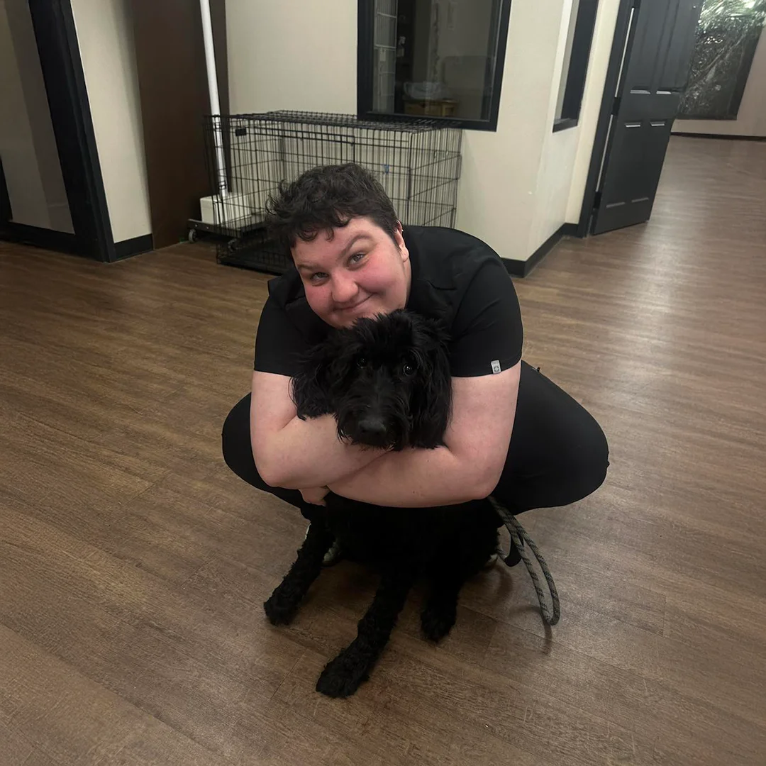 Veterinary staff member crouched and hugging a black dog in a hallway at Animal Medical and Surgical Hospital.