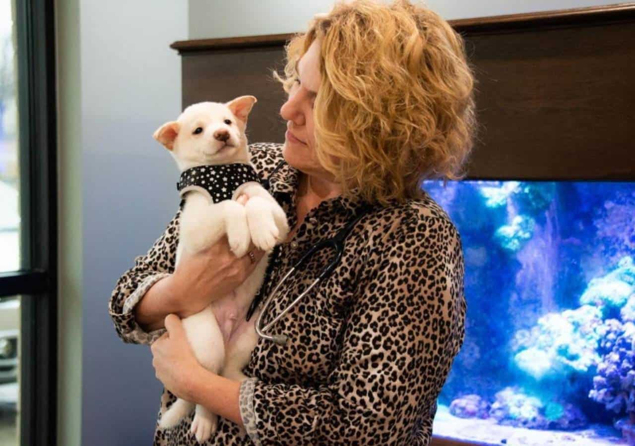 holding a small white dog in front of a fish tank